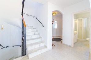 Eine Treppe mit Handlauf, ein runder Teppich und ein Duschbereich mit Glastür.