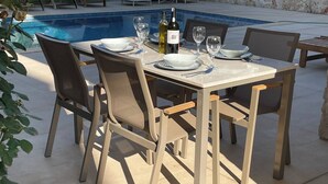 A dining table set outdoors with chairs, a pool in the background, and a bottle of wine. - Sylvana Apartment- a Little Piece of Kalkan Heaven (Kaş)
