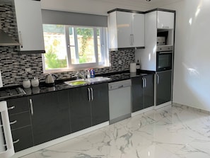 A modern kitchen with dark cabinetry, a dishwasher, and a window with a view of greenery. - Sylvana Apartment- a Little Piece of Kalkan Heaven (Kaş)