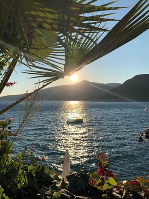 A clear view of a calm sea with a boat, surrounded by greenery and a mountain in the background. - Sylvana Apartment- a Little Piece of Kalkan Heaven (Kaş)