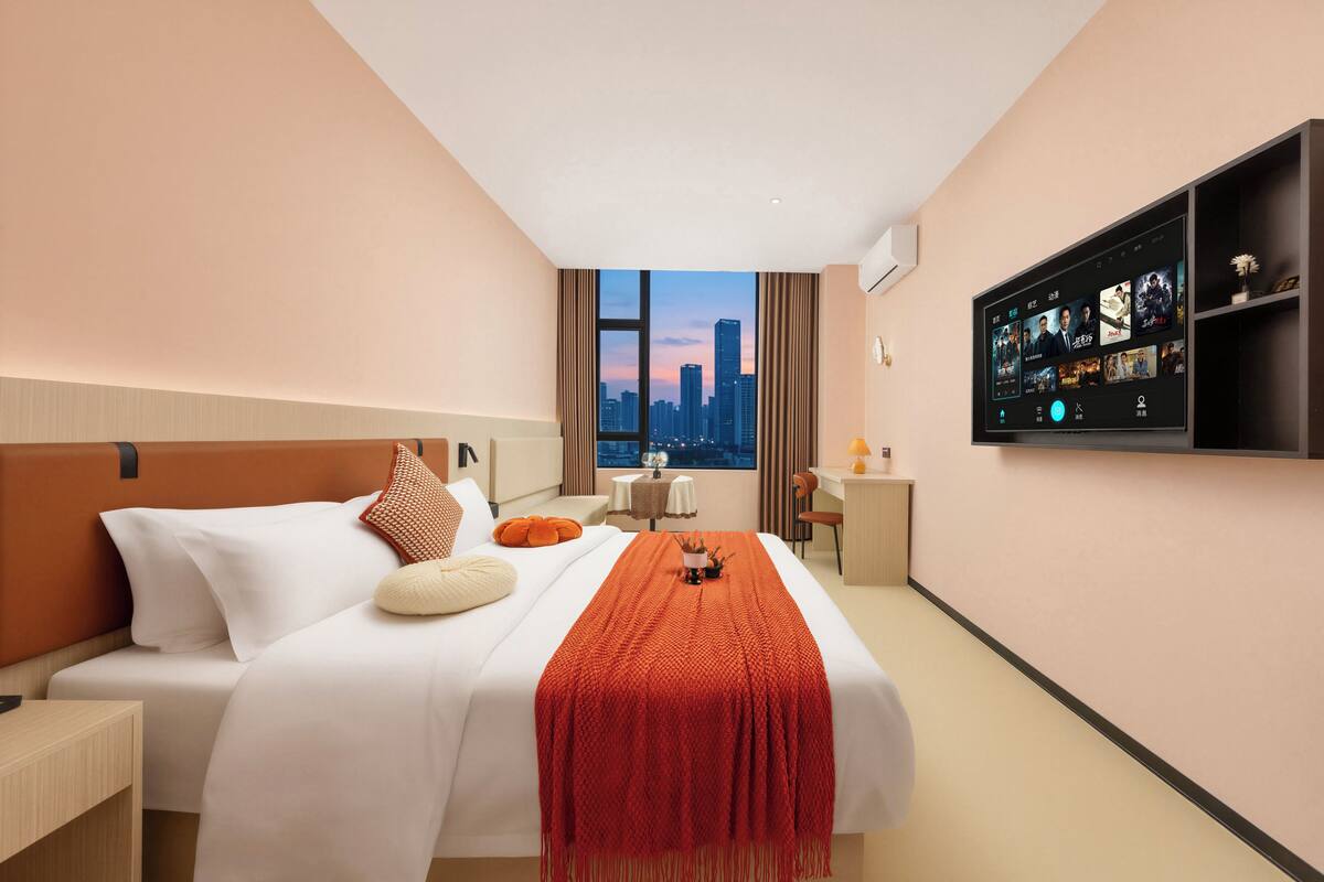 A hotel room with a bed, a desk, a chair, a TV, and a window with a city view.