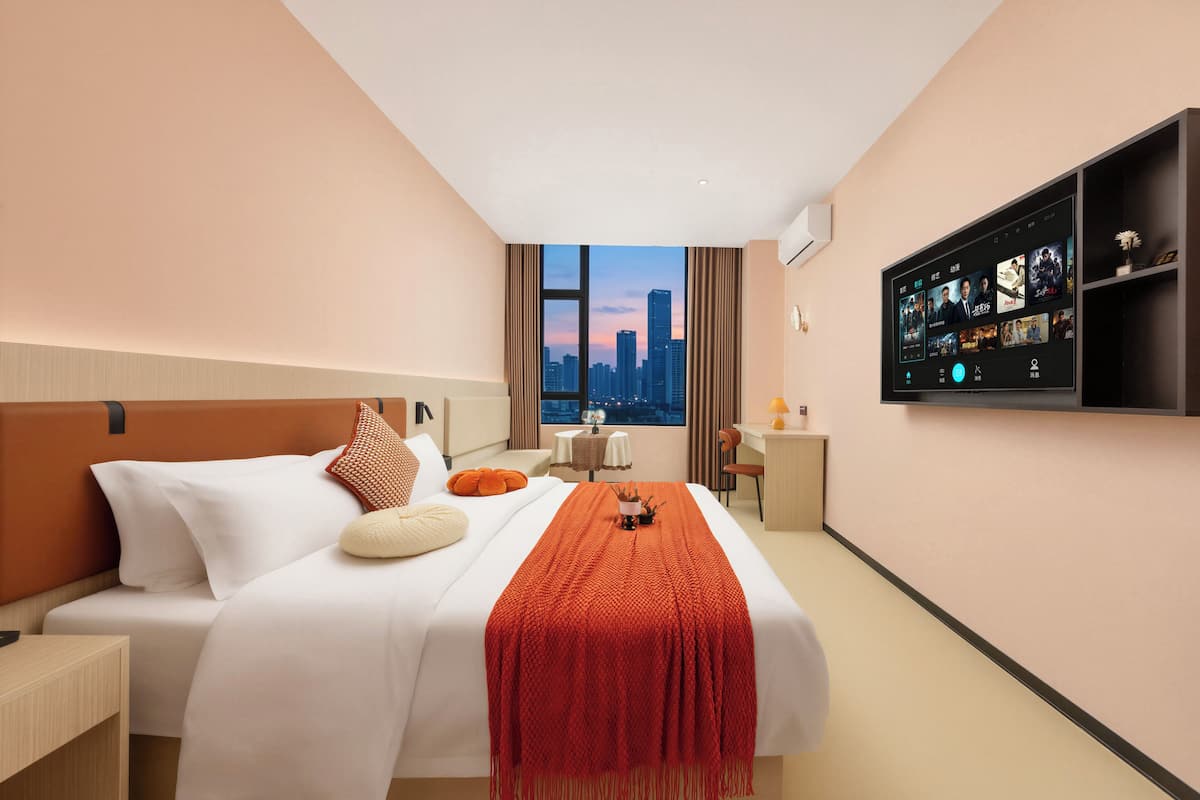 A hotel room with a bed, a desk, a chair, a TV, and a window with a city view.