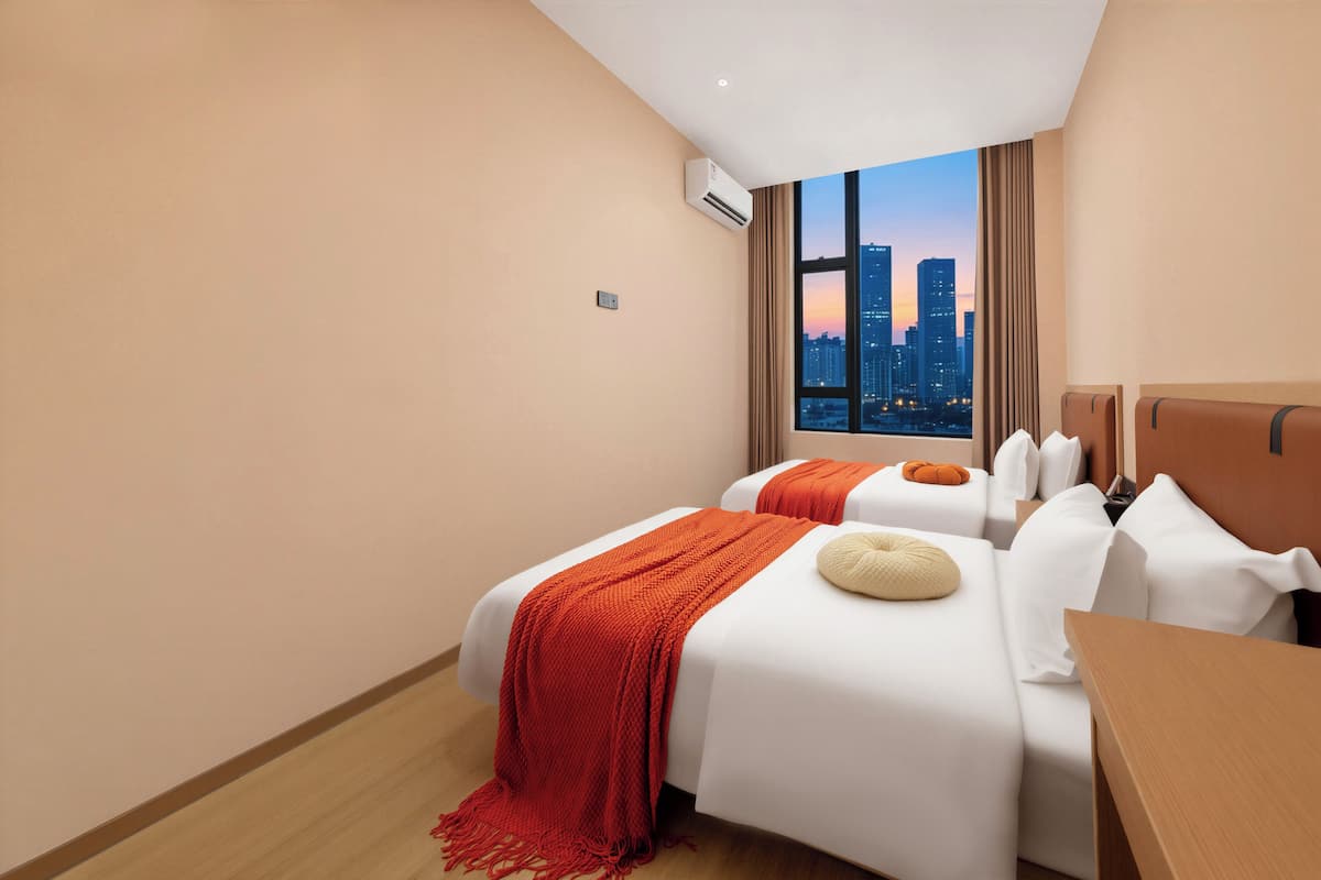 A hotel room with two beds, a wooden floor, a city view, and an air conditioning unit.