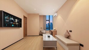 Una sala de estar moderna con un televisor de pantalla plana, un sofá, una mesa de centro y vistas a la ciudad a través de amplias ventanas.