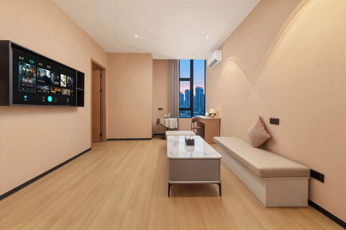 A modern living room with a flat-screen TV, a sofa, a coffee table, and a city view through large windows.