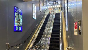 Una escalera mecánica en el interior de un edificio comercial, con pantallas digitales y señalización en las paredes.