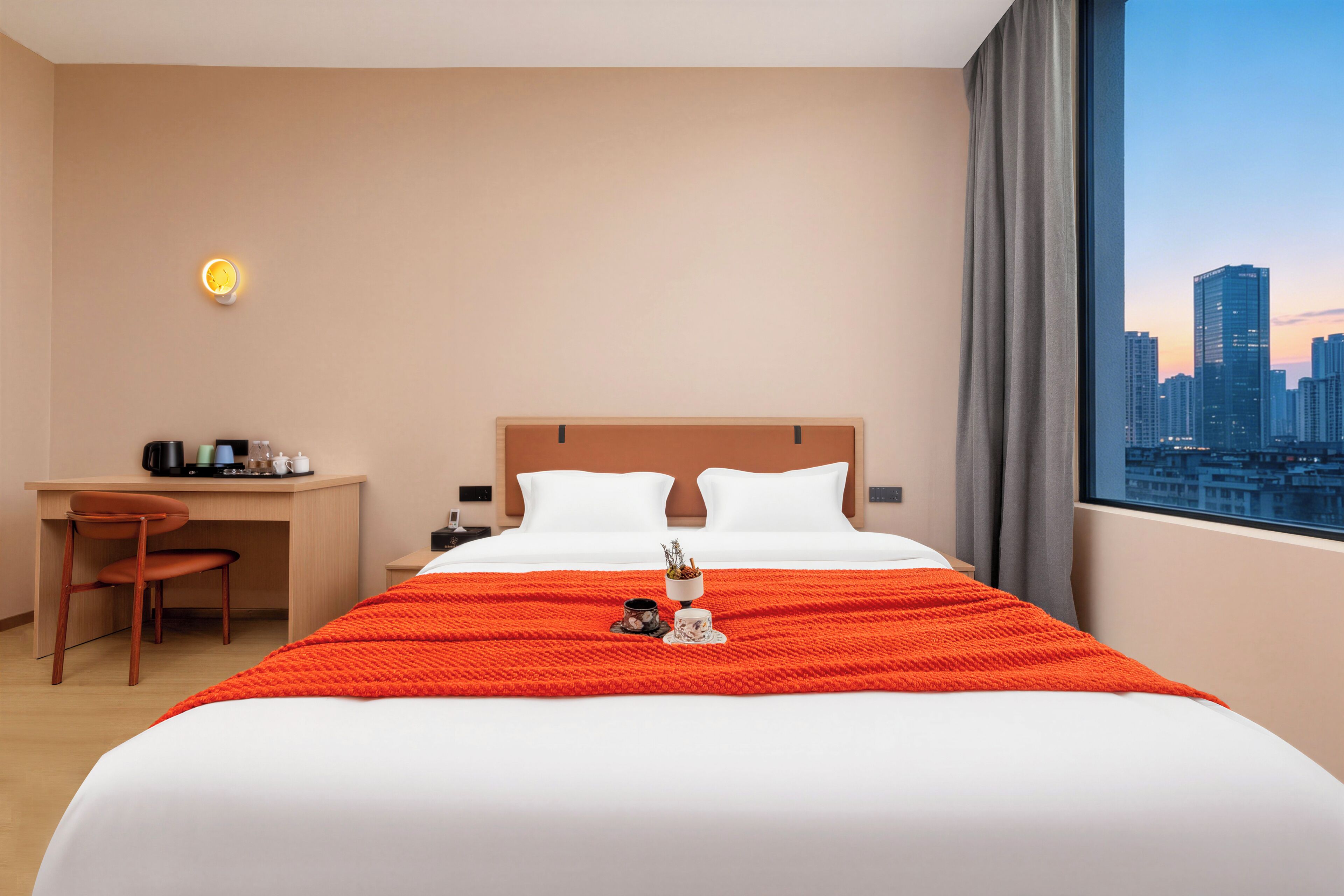 A hotel room with a bed, a desk, a chair, and a city view.