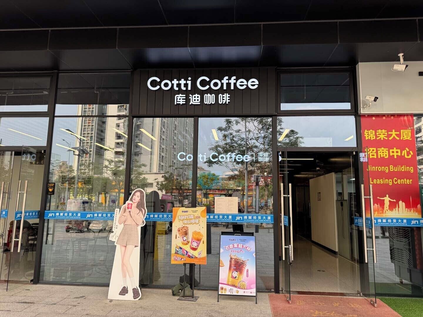 Een winkelgevel met een bord waarop 'Cotti Coffee' staat en een grote poster die een drankje promoot.