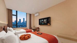 Habitación de hotel con dos camas, vista a la ciudad, televisor montado y una pequeña mesa con una silla.