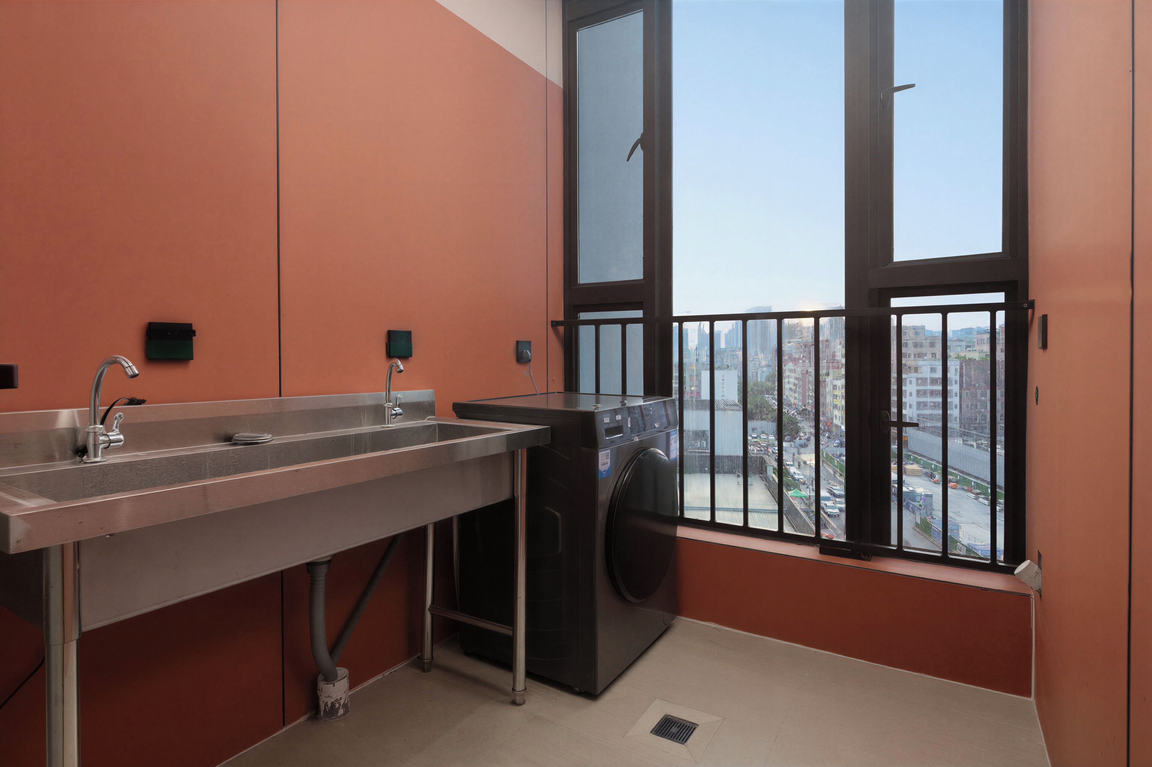 A compact bathroom with a sink, a washing machine, and a window with a view of a cityscape.