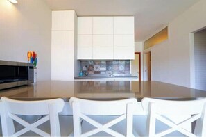 A modern kitchen with white cabinetry, a central island, and a dining area with white chairs. - When all is silent, the sea speaks: beachfront with garden and patio (Salina Bamba)