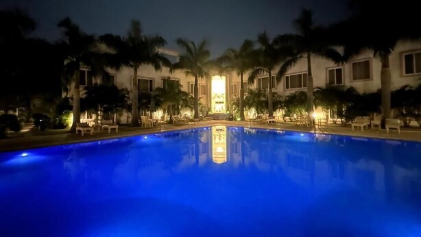 Una vista notturna di una piscina con palme e un edificio sullo sfondo.