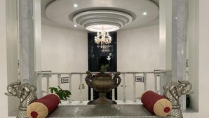 Una hall con un divano decorato, un'ampia urna e due statue di elefanti.