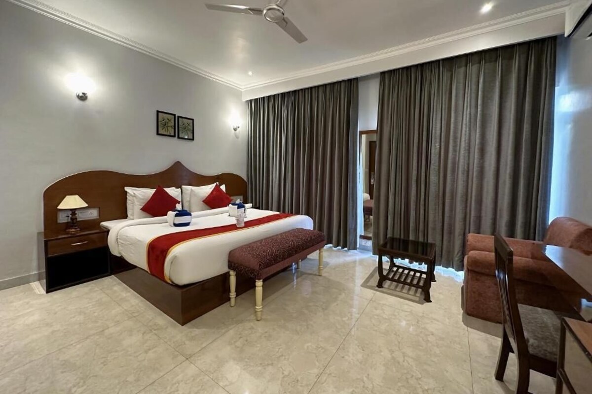 A hotel room with a bed, bedside table, lamp, bench, chair, and a ceiling fan.