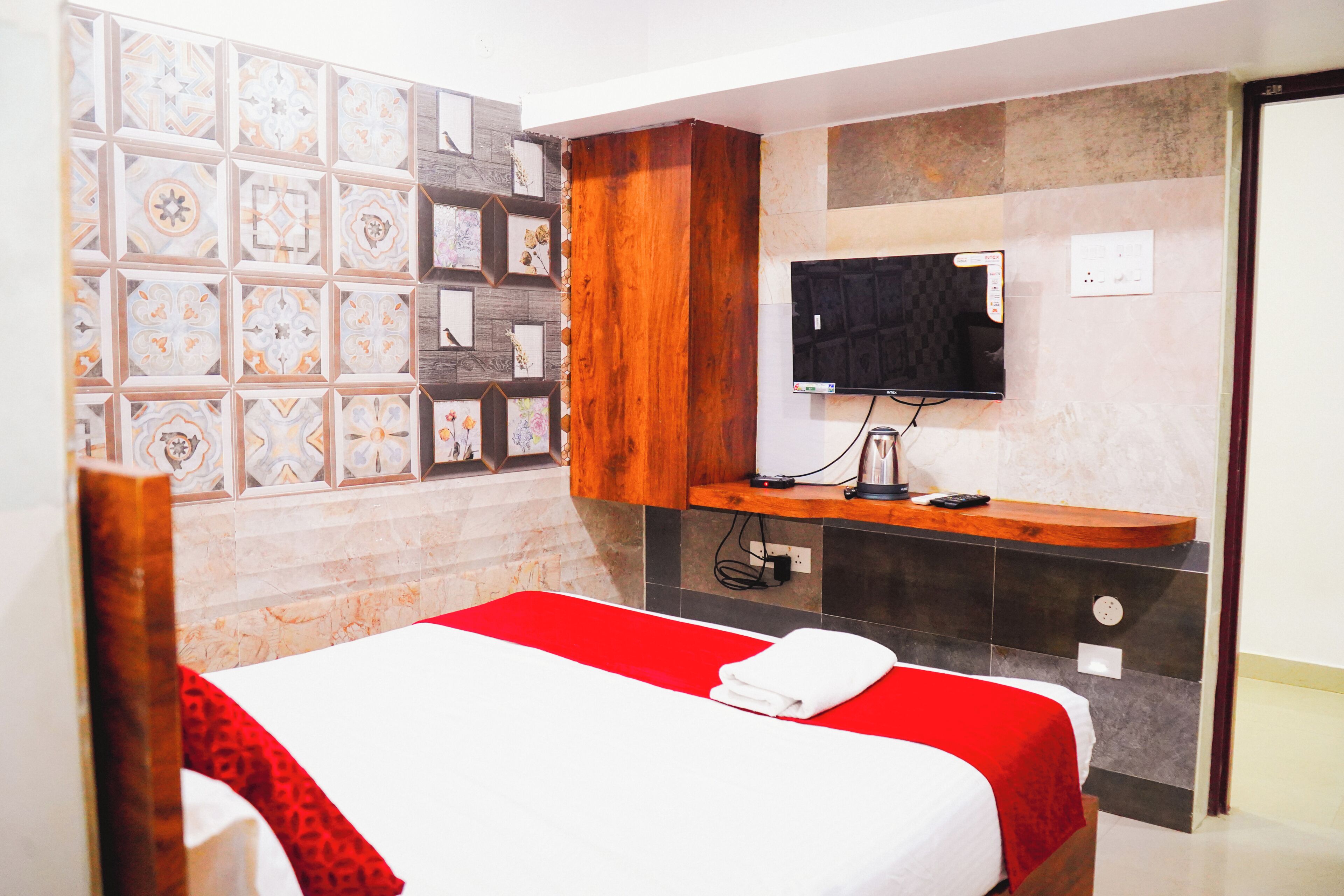 A hotel room with a bed, a TV mounted on the wall, a wooden cabinet, and a tiled wall with framed pictures.