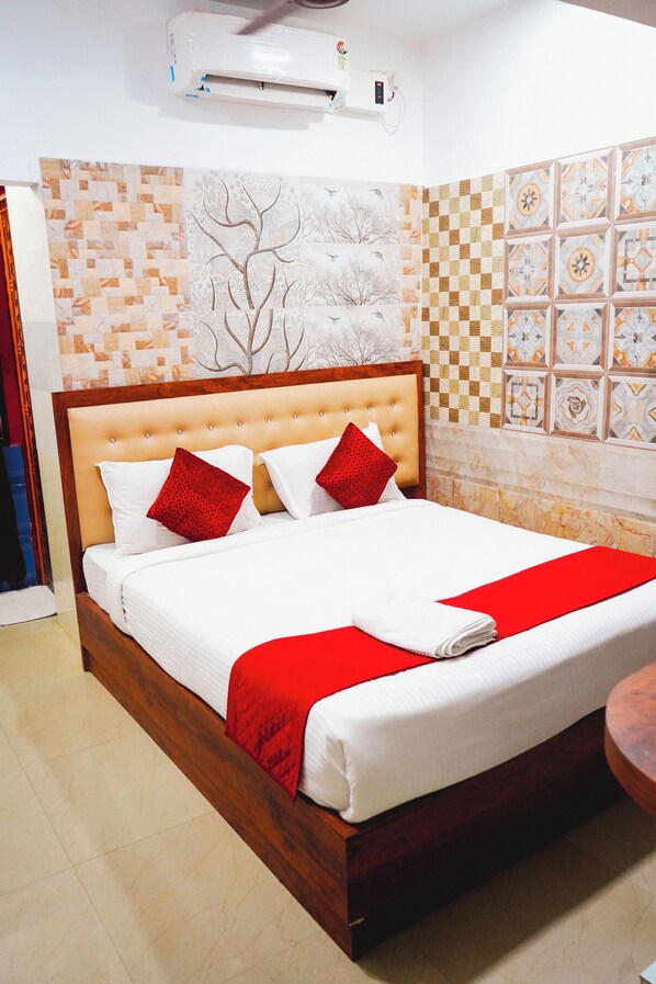 A neatly made bed with a red accent pillow, a wall-mounted air conditioner, and a patterned tile wall.
