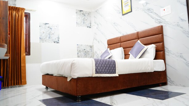 A modern bedroom with a brown upholstered bed, white bedding, and a marble-patterned wall. - SUMI WHITE HOUSE (Thanjavur)
