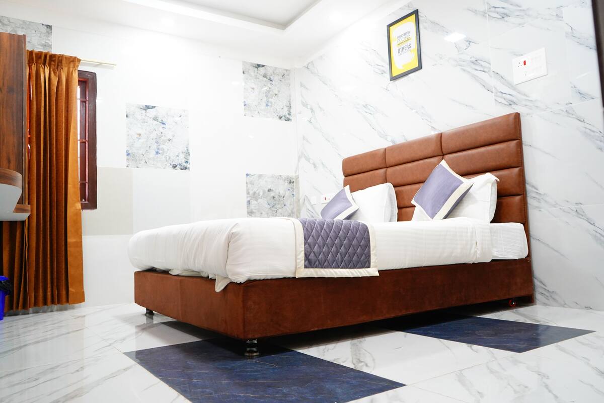Een moderne slaapkamer met een bruin gestoffeerd bed, witte beddengoed en een wand met een marmerpatroon.