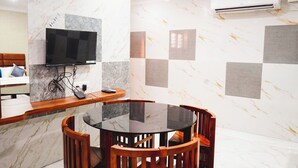A modern room with a marble wall, a flat-screen TV mounted on the wall, a round dining table with chairs, and an air conditioning unit on the wall. - SUMI WHITE HOUSE (Thanjavur)