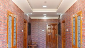 A hallway with brick walls, wooden doors with glass panels, and recessed ceiling lights. - SUMI WHITE HOUSE (Thanjavur)