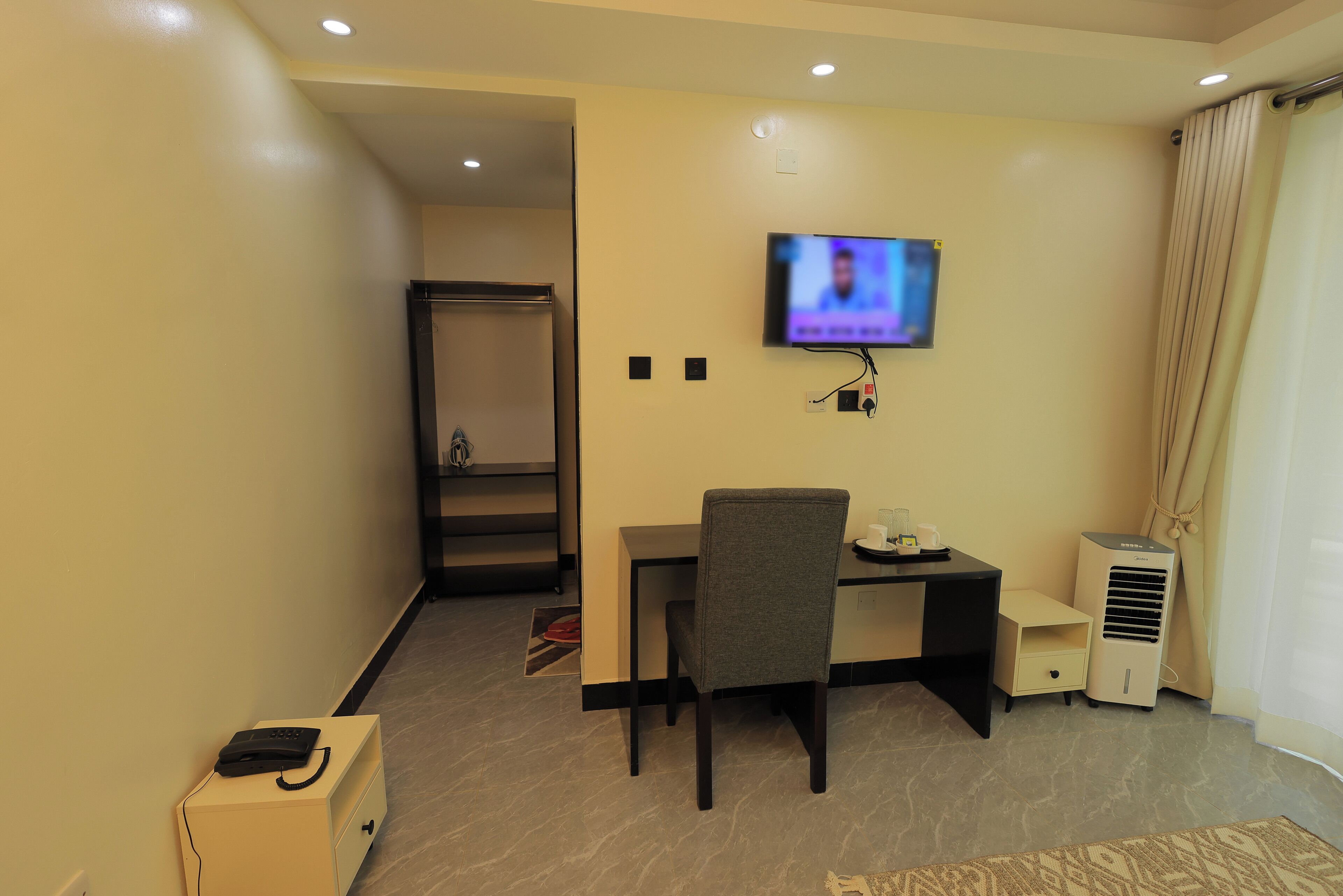 Una habitación de hotel con escritorio, silla, televisor, aire acondicionado y armario.