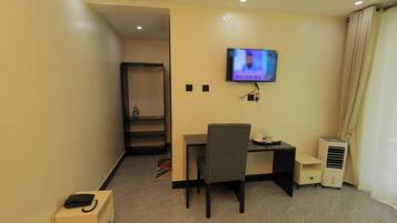 Una habitación de hotel con escritorio, silla, televisor, aire acondicionado y armario.