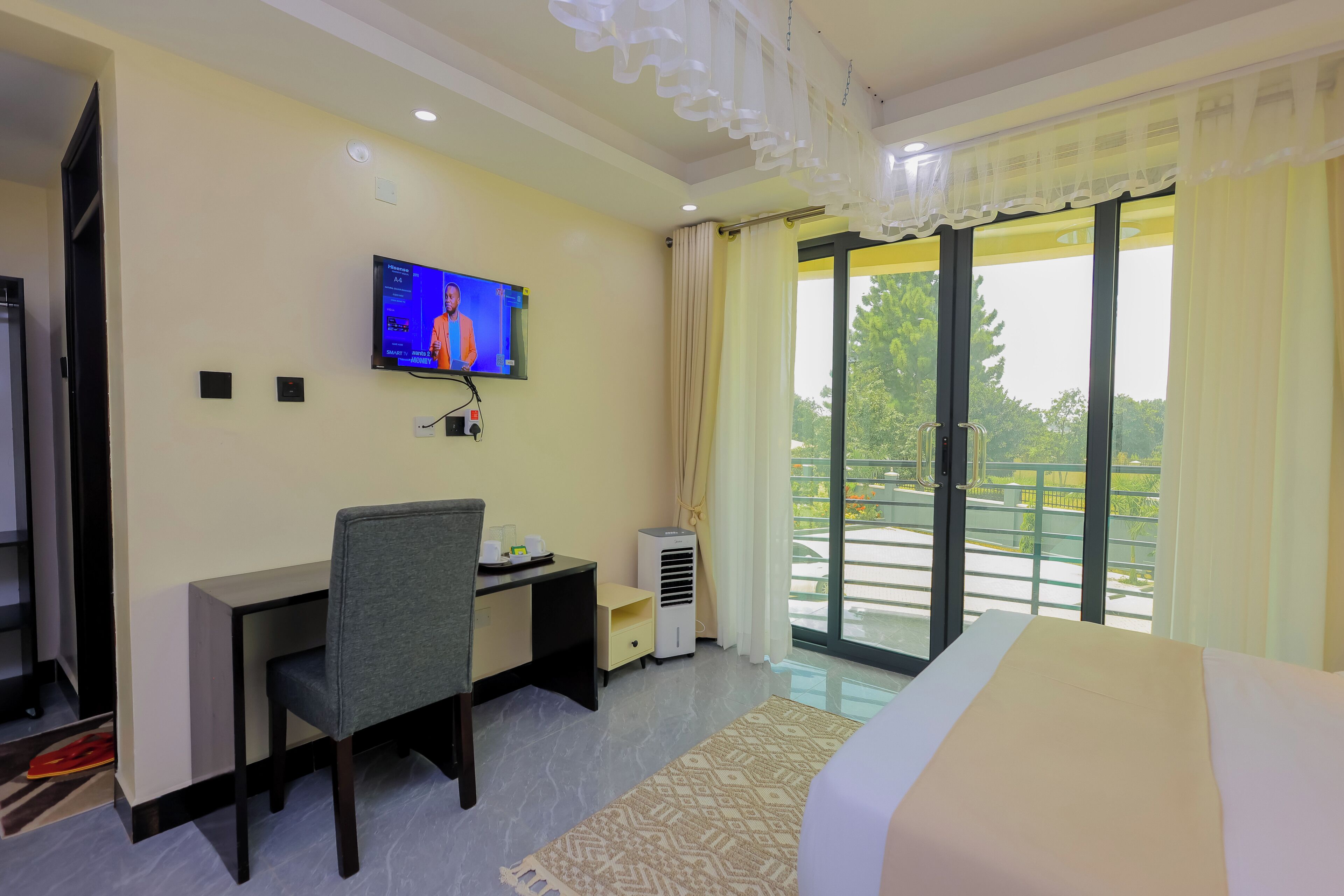 Una habitación de hotel con cama, escritorio y silla, televisión, ventana con cortinas y balcón.