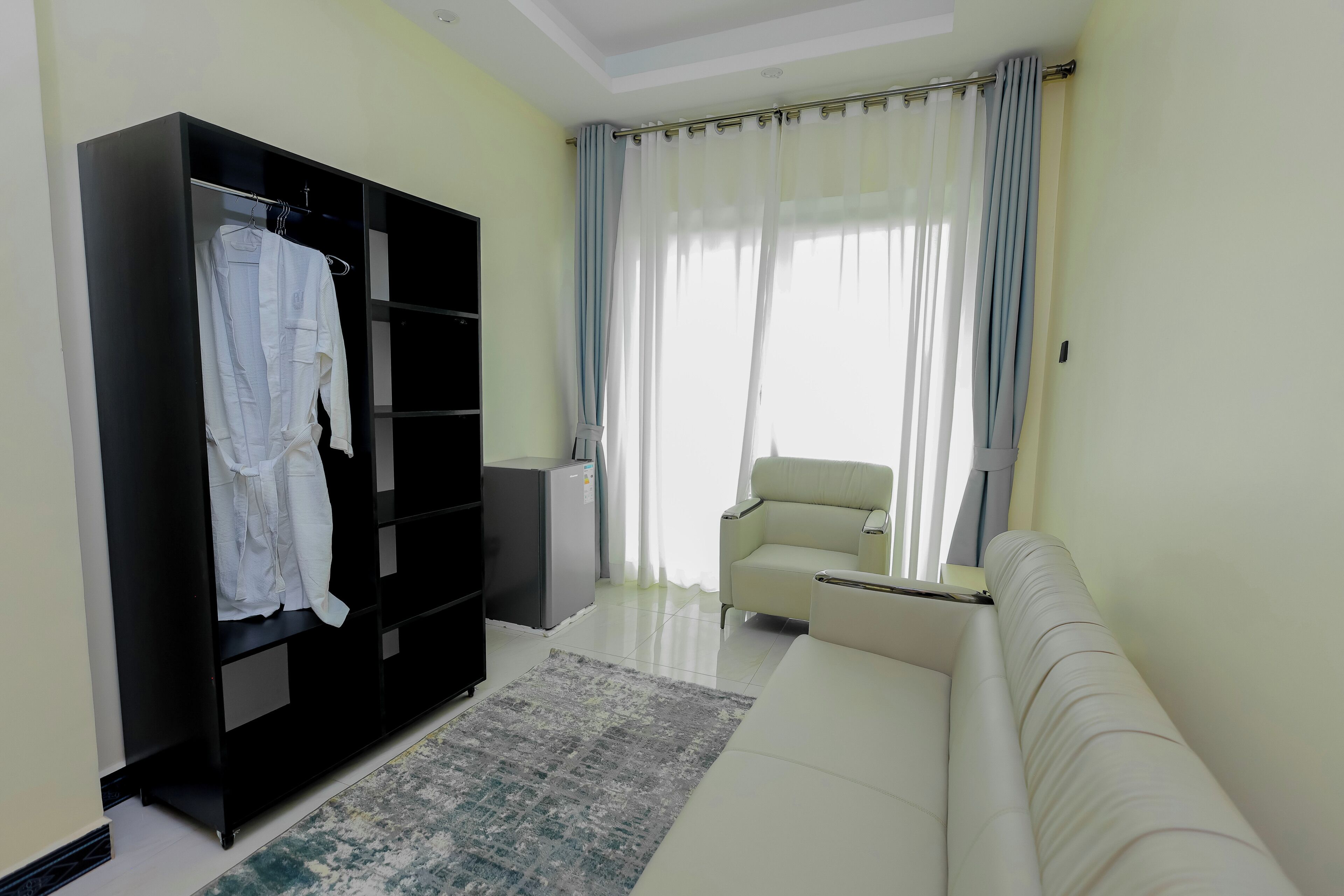 A living room with a sofa, a black wardrobe, a white chair, and a window with curtains.