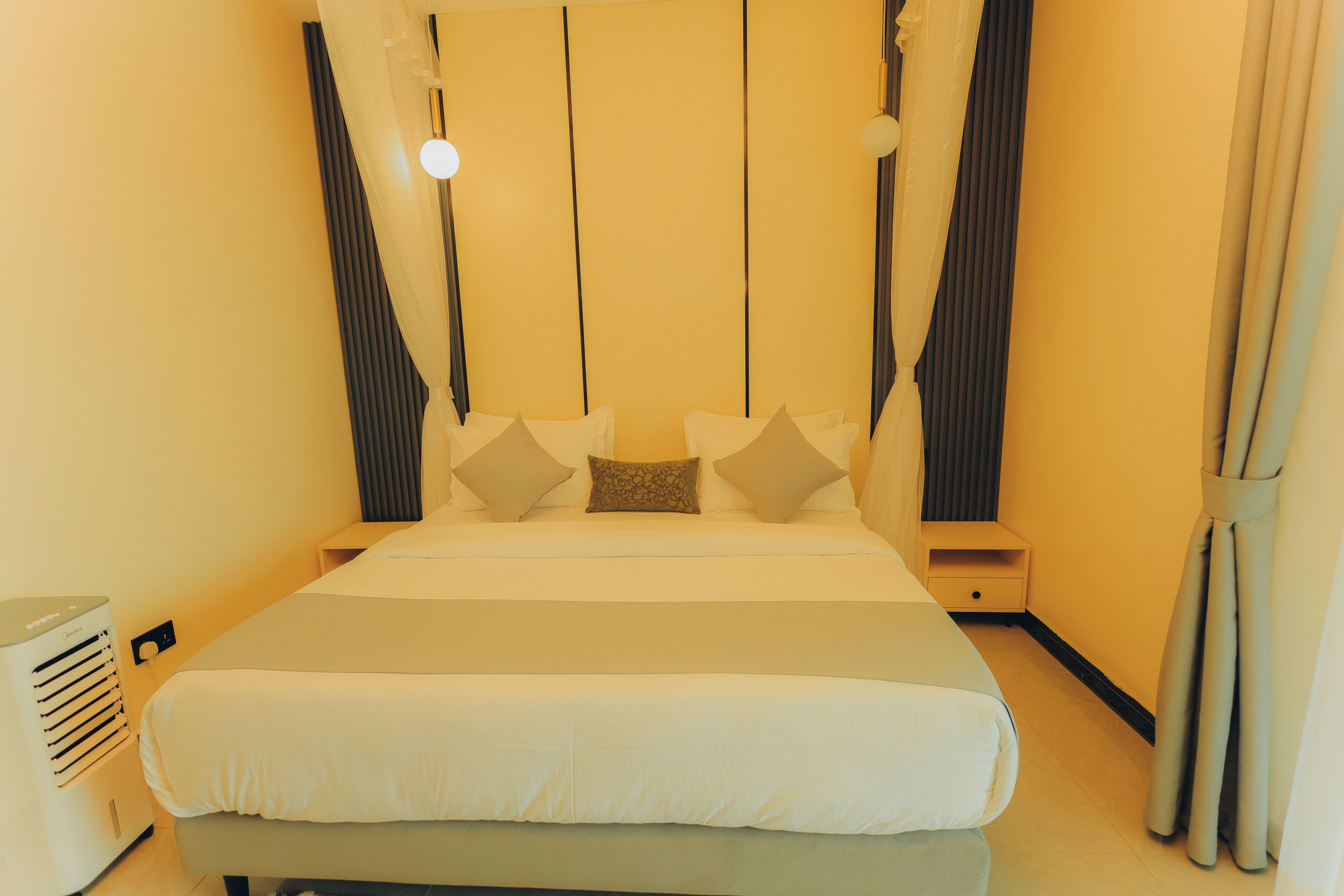 Un dormitorio ordenado con cama, almohadas, una mesita de noche y un aire acondicionado de pared.