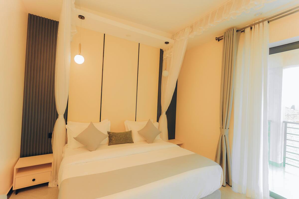 A bedroom with a bed, curtains, a bedside table, and a hanging light fixture.