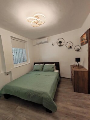 Quarto com cama, janela, ar condicionado, penteadeira de madeira e decorações hexagonais na parede.