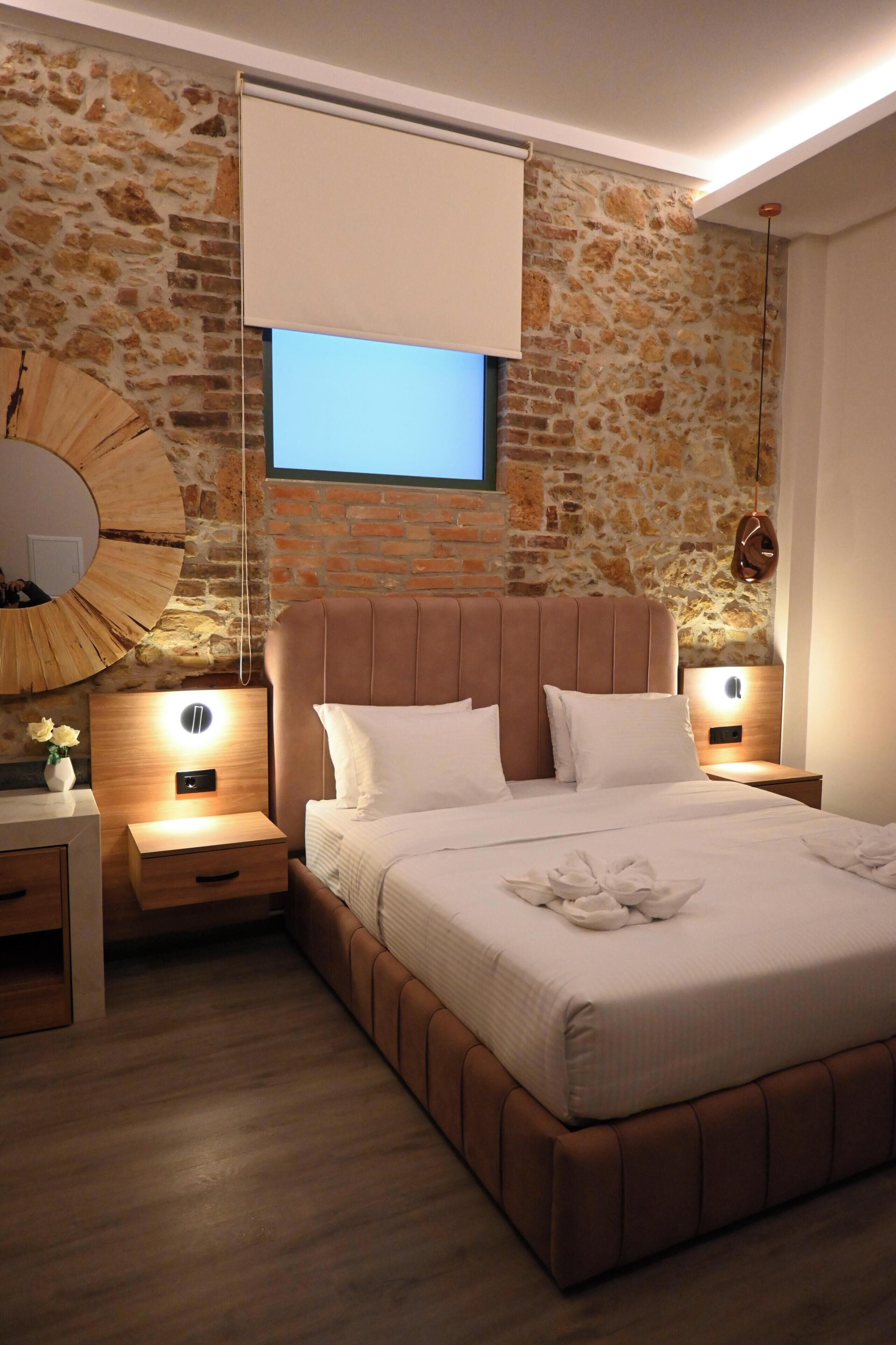 A bedroom with a stone wall, a bed with white bedding, two bedside tables, and a wall-mounted TV.