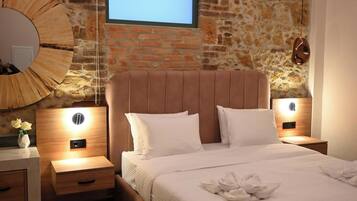 A bedroom with a stone wall, a bed with white bedding, two bedside tables, and a wall-mounted TV.