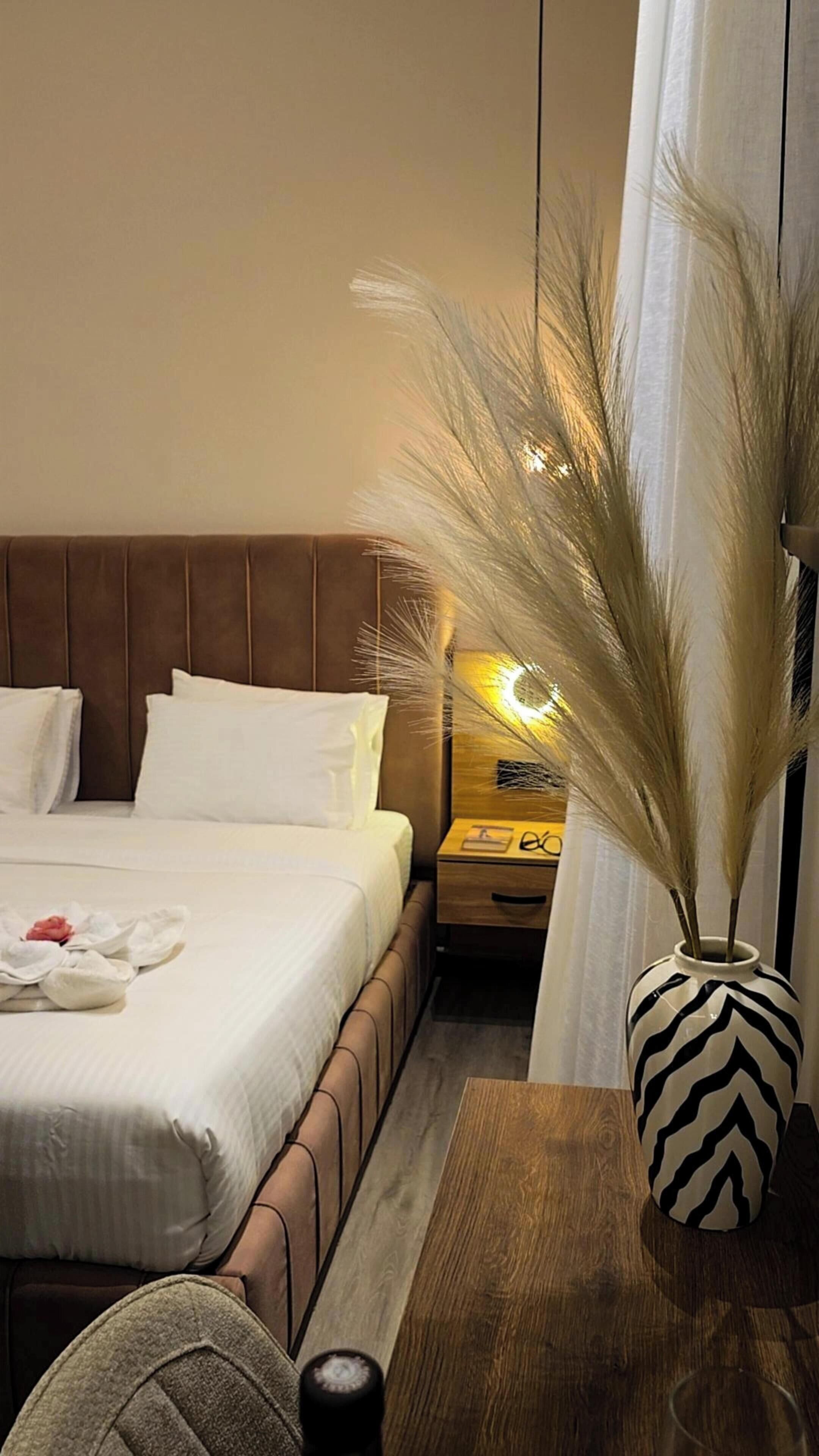 A hotel room with a bed, bedside table, lamp, and a decorative vase.