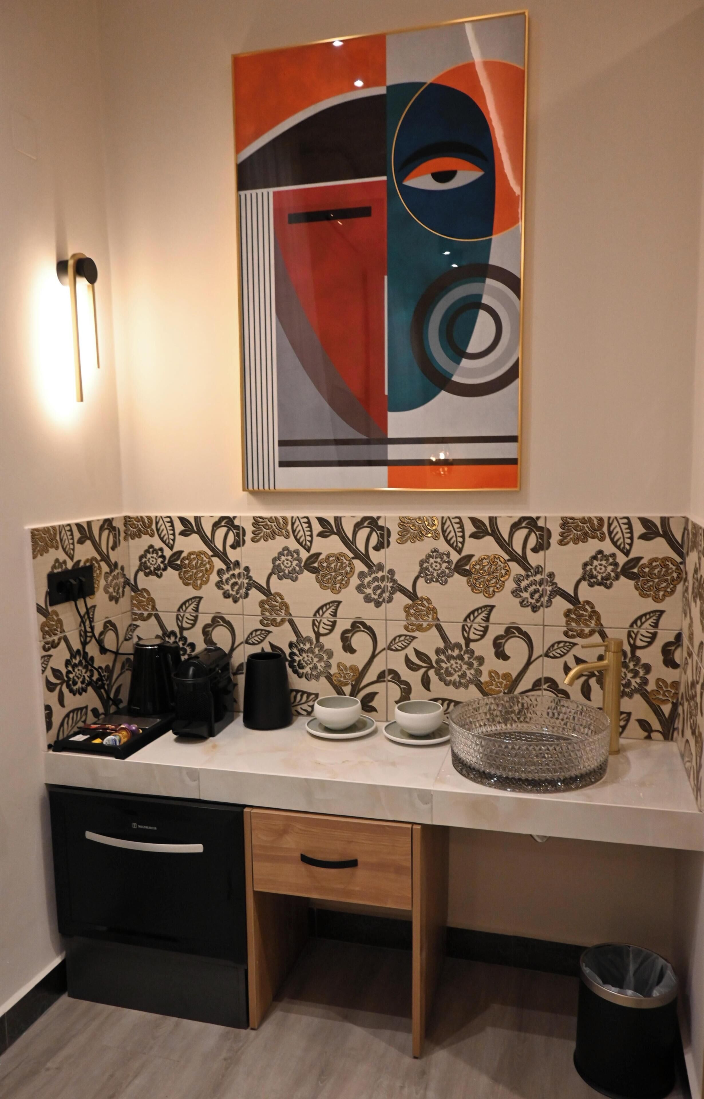 Una cocina con una encimera, un fregadero, una cafetera, un hervidor y un cubo de basura.