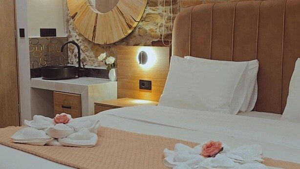 A hotel room with a large bed, a round mirror, a wooden headboard, a nightstand, and a bathroom with a sink and mirror. - Apon City Residence (Chania)