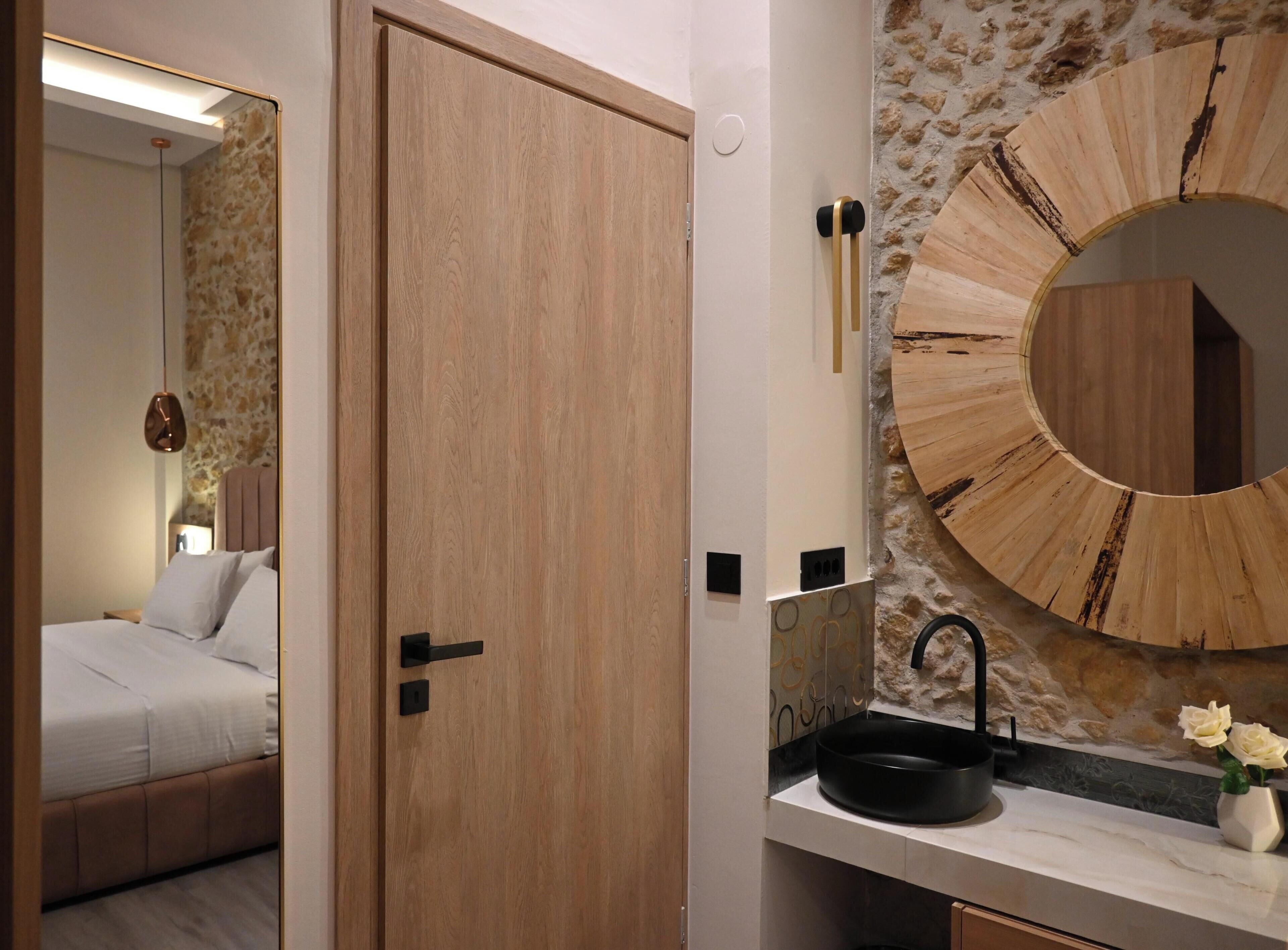 A modern bathroom with a wooden door, a round mirror, a black sink, and a stone wall.