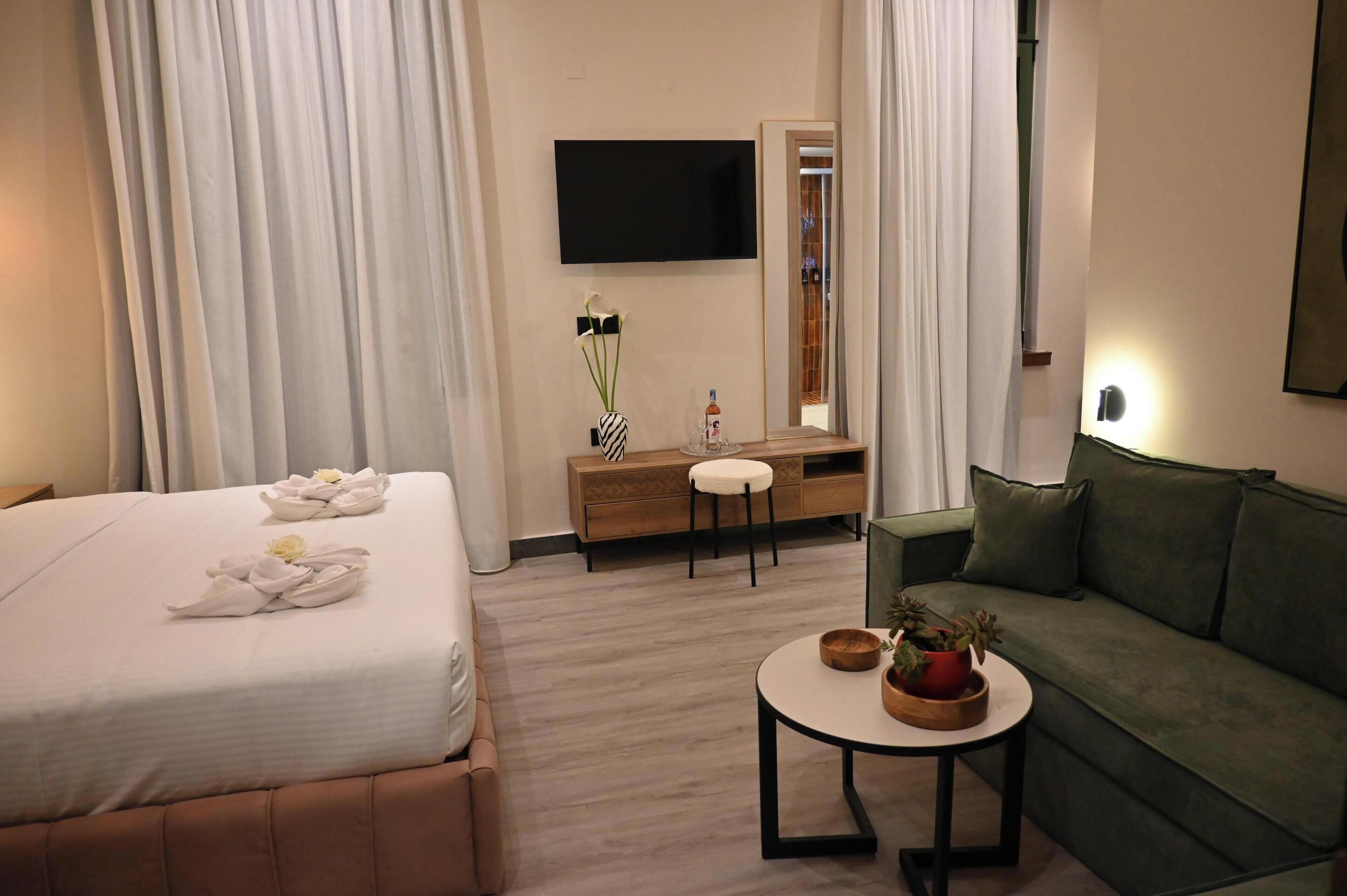 A hotel room with a bed, a sofa, a small table, a TV, a mirror, and a dresser.