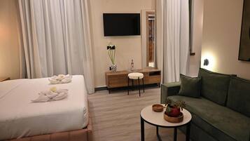 A hotel room with a bed, a sofa, a small table, a TV, a mirror, and a dresser.