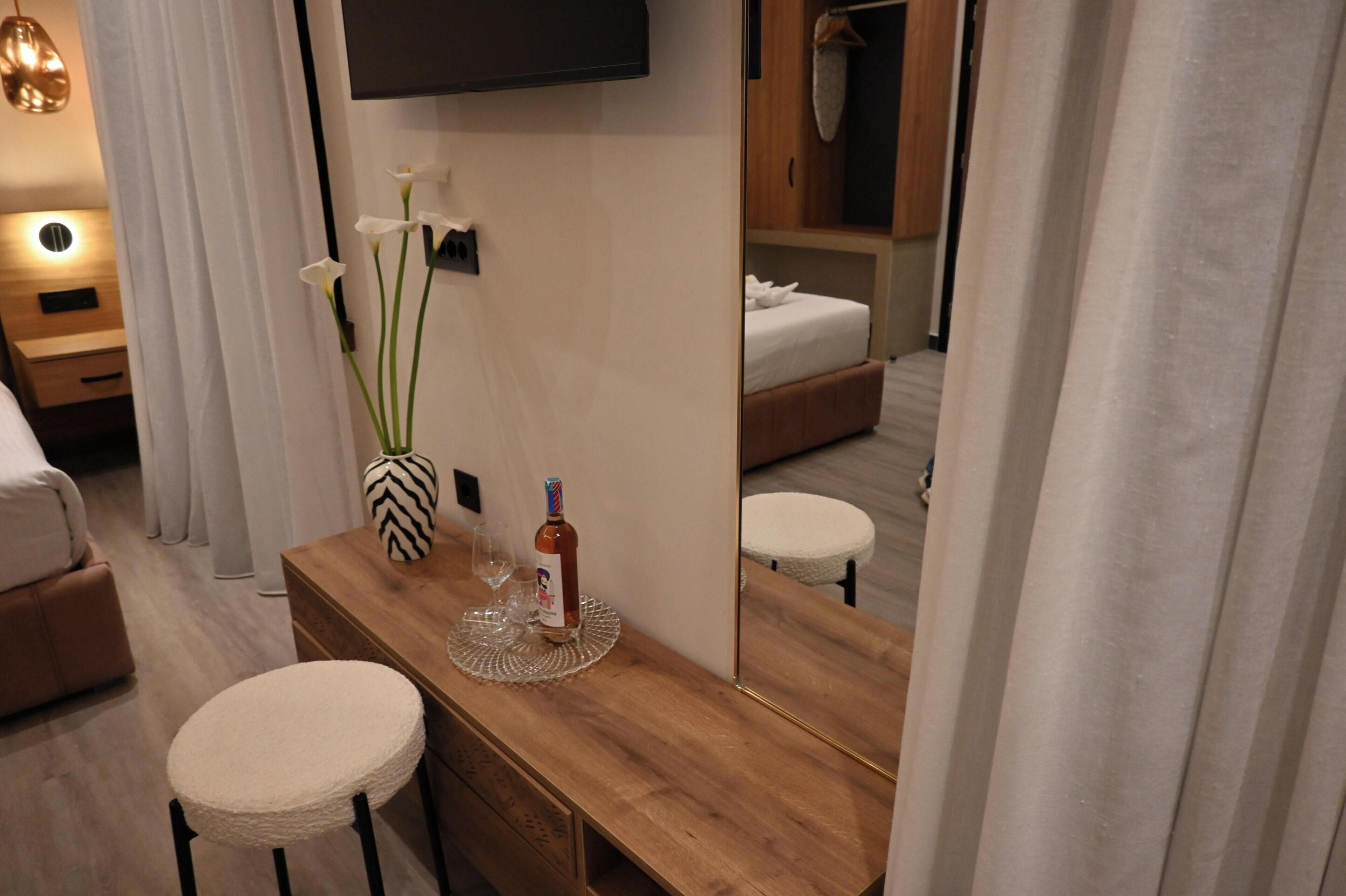 Ein Hotelzimmer mit einem Holztisch, einem Spiegel, einer Spirituosenflasche und weißen Blumen.