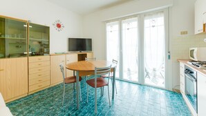 A kitchen with a dining table, chairs, a TV, cabinets, and a microwave. - Anna Flat (Lido di Jesolo)