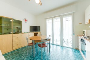 A kitchen with a dining table, chairs, a TV, cabinets, and a microwave. - Anna Flat (Lido di Jesolo)