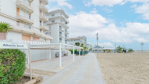 A beachfront hotel with a sign reading 'Alberto Sordi,' outdoor seating, and a sandy beach in the background. - Anna Flat (Lido di Jesolo)