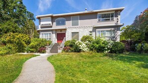 A two-story house with a stone facade, a red door, and a front yard with a pathway leading to the entrance. - Room-cozy & Huge Primary Suite Near UBC (Vancouver)