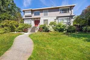 A two-story house with a stone facade, a red door, and a front yard with a pathway leading to the entrance. - Room-cozy & Huge Primary Suite Near UBC (Vancouver)
