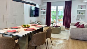 Een moderne woonkamer met een eethoek, een bank en een aan de muur bevestigde televisie.