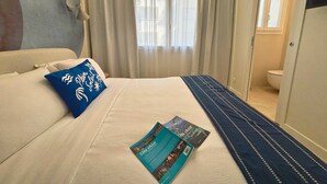 Een hotelkamer met een bed, een raam met gordijnen, een deur naar een badkamer en een tijdschrift op het bed.
