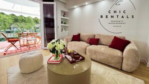 Een moderne woonkamer met een beige bank, rode kussens, een glazen salontafel en een bord met de tekst 'The CHIC RENTALS PROPERTY MANAGEMENT FRANCE'.