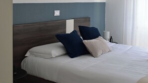 Una habitación de hotel con una cama, una mesita de noche, una lámpara y un ventanal con cortinas.