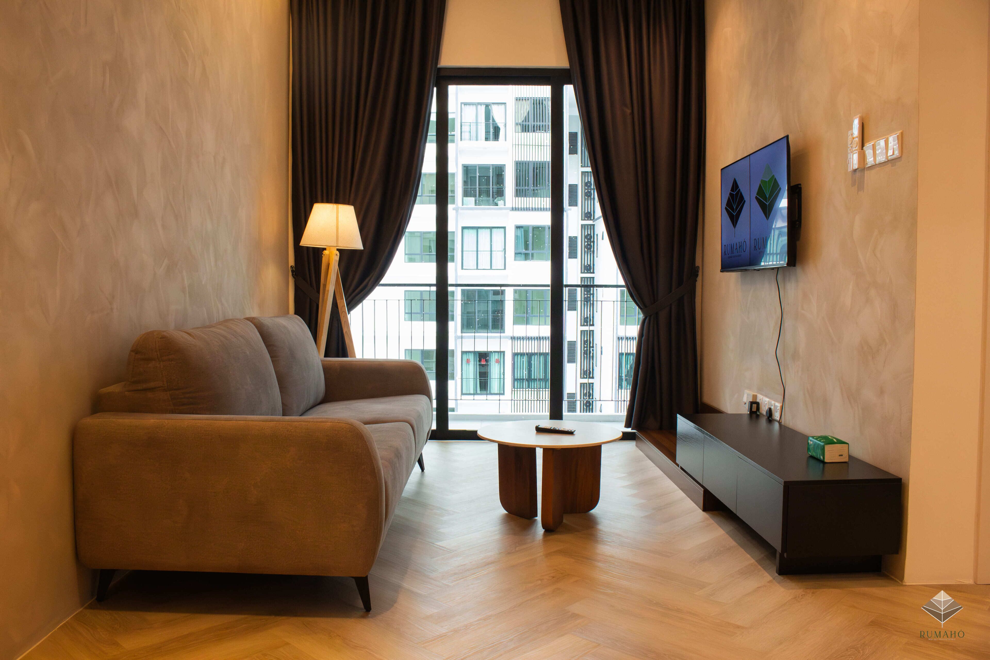 Een moderne woonkamer met een bank, een lamp, een salontafel, een televisie en uitzicht op een gebouw door grote ramen.